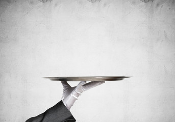 Hand of butler holding empty metal tray against concrete background