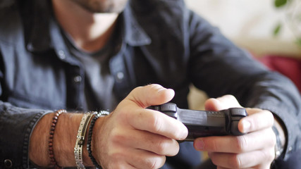 Attractive young man using joystick or joypad for videogames, sitting on couch at home in his living room, staring at TV screen