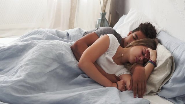 Multiracial couple lying in bed and sleeping while embracing each other. Young family concept