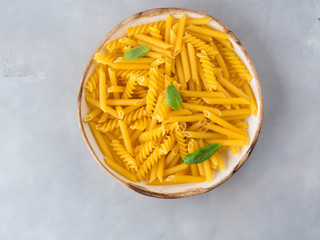 Italian raw short pasta in a dish with basil leaves on gray background