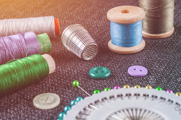 Sewing accessories: spools of threads, needles, thimble, buttons, on the textured fabric surface illuminated by warm light (toned)