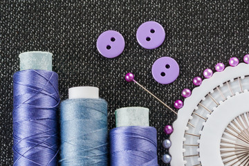 Sewing accessories: spools of threads, needles, buttons, on the textured fabric surface (flat view)