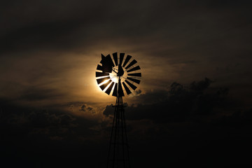 A windmill against a setting sun and storm clouds.