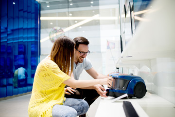 Attractive young couple is looking for a new vacuum cleaner in the electronics store.