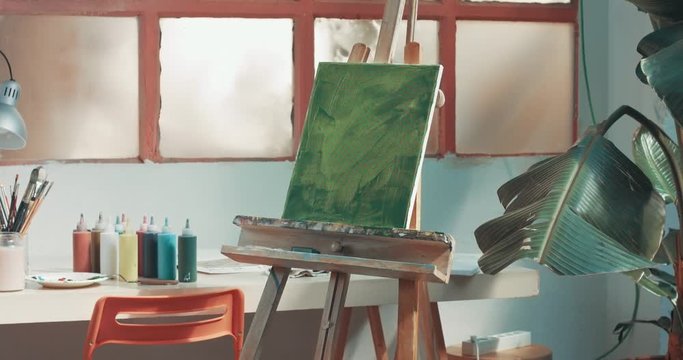 Pan video of an artist's studio with brushes, pencils, markers and other tools and an abstract green painting on an easel