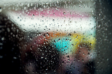 Drops of rain on a window pane, people in background. Shallow depth of field.