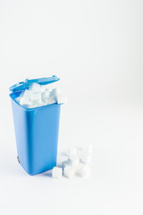 Blue trash can full of sugar cubes, white background