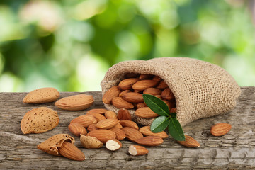 Almonds with leaf in bag from sacking on a wooden table with blurred garden background