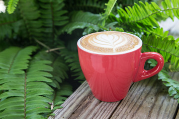 coffee cup on wood table with fern leaf background