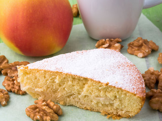 a piece of Charlotte on parchment, nuts, apple and cup of tea. Apple pie  decorated with icing sugar