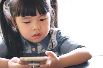 Asian children cute or kid girl wearing jeans with looking smartphone screen for vdo clip or...