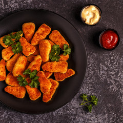 Chicken nuggets with sauces on dark background.