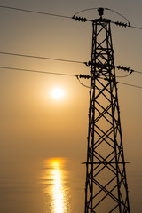 High-voltage power line against the backdrop of the sea at sunset