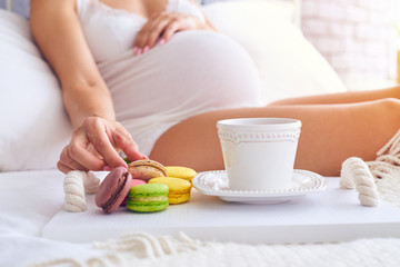 Fototapeta na wymiar Hand of pregnant woman holding a macaroon on bed