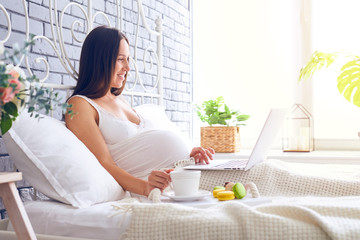 Obraz na płótnie Canvas Pregnant woman with laptop and tray with breakfast sitting in bed