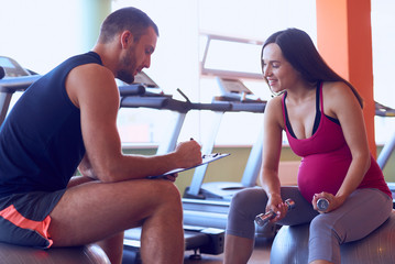 Sportive pregnant woman noting results with personal trainer