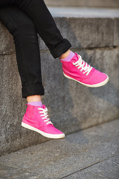 Female feet in pink sneakers on stone wall