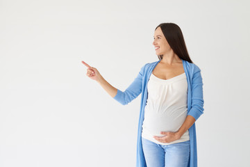 Happy young pregnant woman pointing at copy space in studio