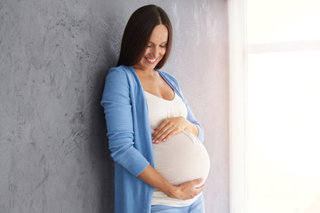 Smiling pregnant woman looking at belly while posing in studio