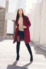 young beautiful stylish woman in claret coat, street style, spring summer trend, dark skirt, beige sweater, flirty