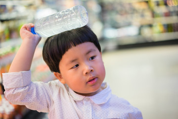 A boy is choosing cold bottle of water or beverage on shelves in supermarket store.