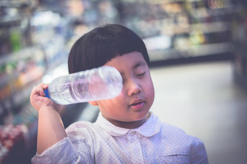 A boy is choosing cold bottle of water or beverage on shelves in supermarket store.