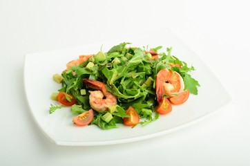 Salad with shrimps, avocado, cherry tomatoes and arugula on a plate isolated on white background