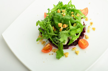 Salad with beet, cheese, cherry tomatoes, arugula and walnut on a plate isolated on white background