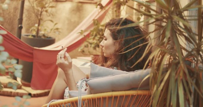 Beautiful young woman with long curly reddish brown hair relaxing in her backyard garden smoking a cigarette