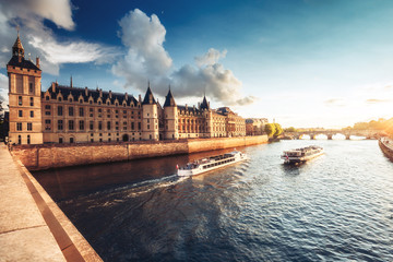 Dramatic sunset over river Seine and Conciergerie in Paris, France, with cruise boats and Pont...