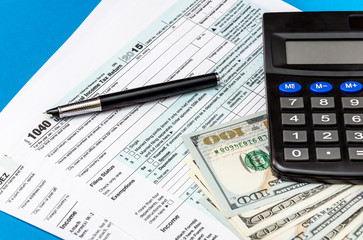 Tax form with calculator, money and pen on a blue background. Business concept. Top view.