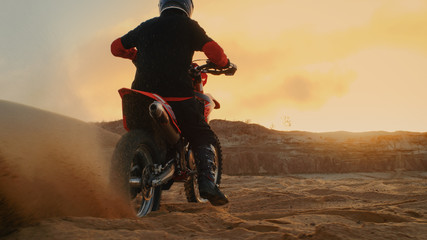 Professional Bike Rider Blasts-off on His FMX Motorcycle Over Sandy Off-Road Track. Scenic Sunset is on the Background.