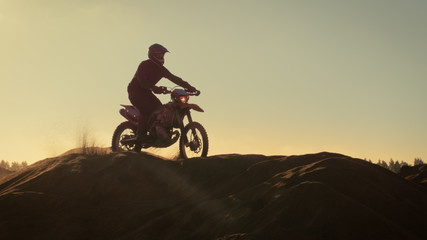 Fototapeta na wymiar Professional Motocross Motorcycle Rider Drives Over the Dune and Further Down the Off-Road Track. It's Sunset.