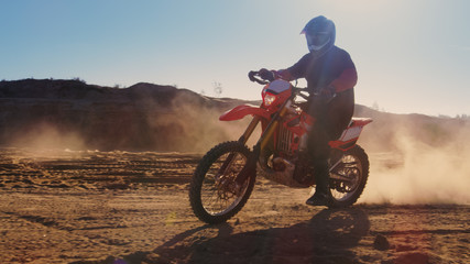Side View Footage of the Professional Motocross Motorcycle Rider Driving on the Dune and Further Down the Off-Road Track. It's Sunset and Track is Covered with Smoke/ Dust/ Dirt. © Gorodenkoff