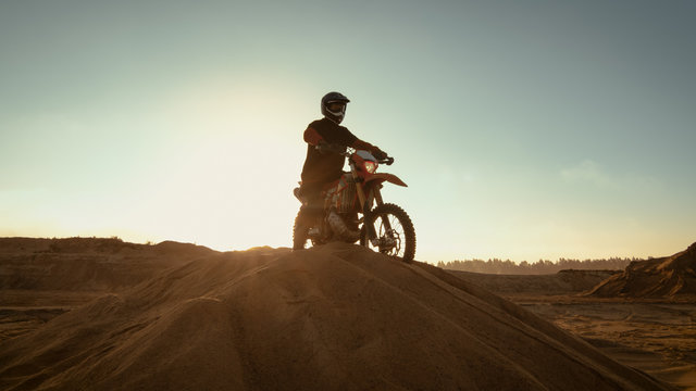 Professional Motocross Rider on FMX Motorcycle Stands on the Sand Dune and Overlooks Whole Extreme Off-Road Terrain that He Gonna Ride Today.