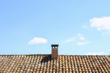 Summer weather. Sunny day with blue sky and some white clouds. Beautiful classic roof with rural tiles. Reddish color. Abstract and colorful building background.