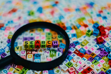 Word "SEARCH" on the magnifying glass with alphabet letter beads background, Search engine optimization concept (added color filter)