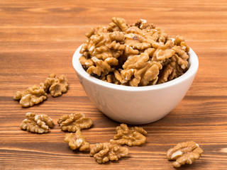 white cups with walnut, bowls with handful of nuts  on a wooden background