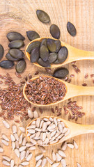 Flaxseed, pumpkin and sunflower seeds in wooden spoons.