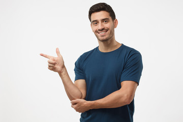 Handsome male in blue t-shirt pointing left with finger isolated on gray background
