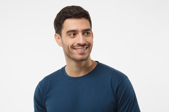 Close up portrait of smiling handsome male in blue t-shirt looking right, isolated on gray background