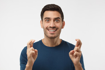 Closeup portrait of hansome caucasian male isolated on gray background, looking at camera, crossing fingers for luck