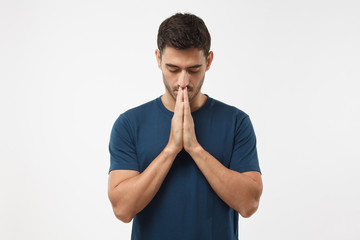 Picture of young guy dressed casually isolated on grey background, having put hands together in prayer or meditation, looking relaxed and calm, dreaming and waiting for all best