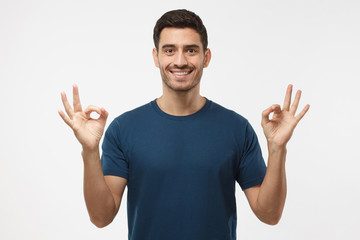 Naklejka premium Portrait of good looking man isolated on grey background smiling, and showing okay sign with both hands, sharing positive experience addressing audience with advice