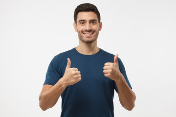 Closeup of young optimistic man isolated on grey background showing thumps up with positive...