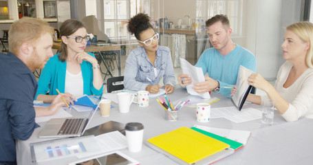 Fototapeta premium Side view of woman holding folder with document and showing it to coworkers while having conference at table in modern office.