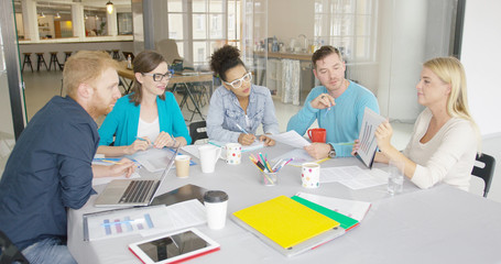 Young casual people watching document with graphic while working together at table and listening to presentation of coworker.