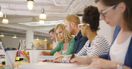 Diverse people posing in row at table on background of modern office and working all together with various documents.