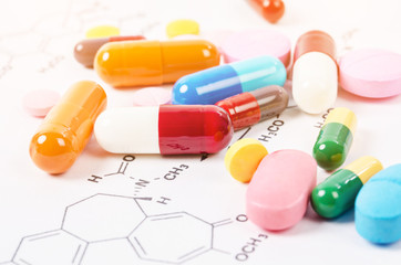 Heap of color pills and tablets on chemical formulas.