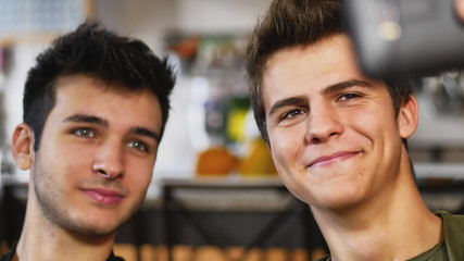 Two handsome young men taking selfie with smartphone on blurry background in apartment.